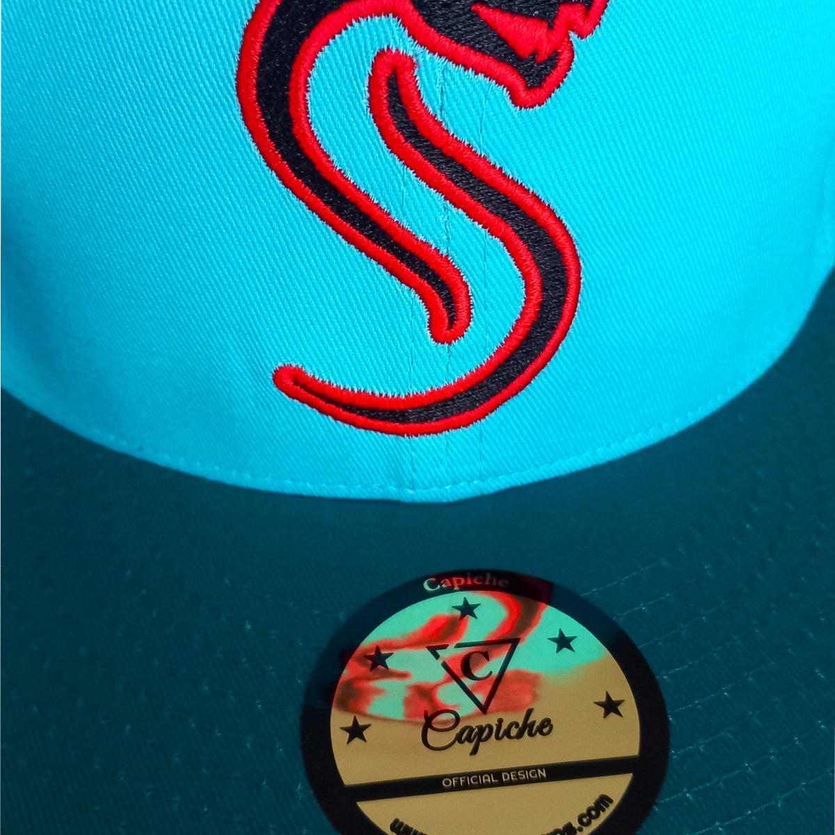 Close up from the red snake logo on a blue snapback from Capiche Caps