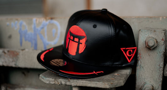Casquette noire de Capiche Caps avec détails brodés rouges, stylisée dans un cadre urbain pour célébrer Kwanzaa et refléter la fierté, la culture et une expression streetwear audacieuse.