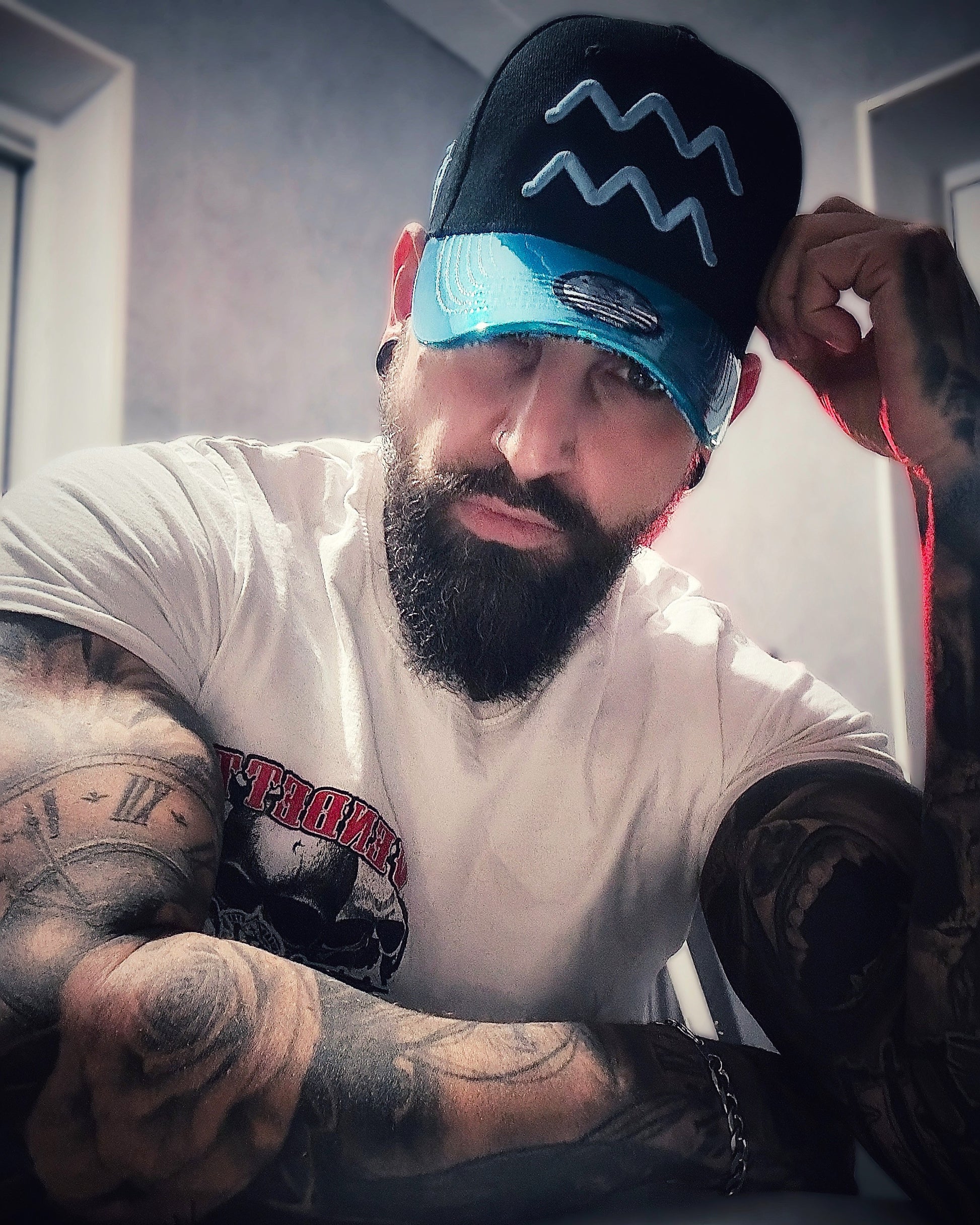 Tattoo model looking into the camera and wearing the black curved cap with blue metallic brim from the high-end headwear brand Capiche 