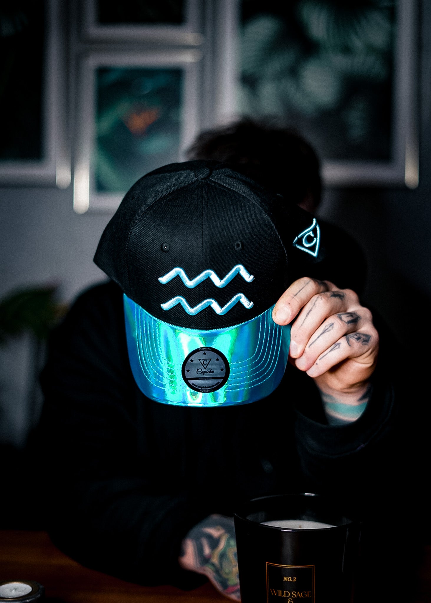 Man sitting and holding the Aquarius curved baseball hat from company Capiche. The hat has a beautiful blue metallic brim