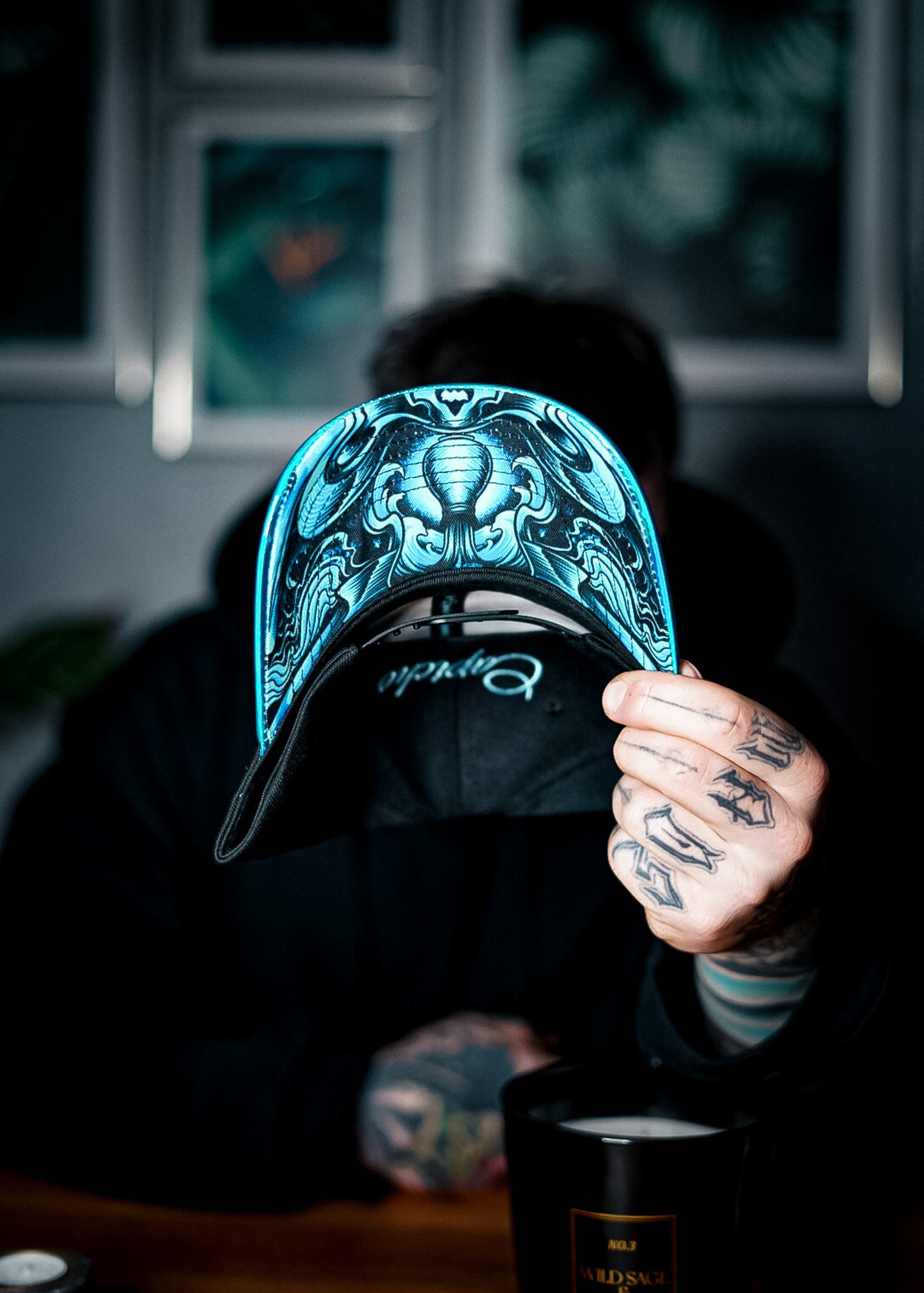 Man with tattoos on his hands holding the aquarius curved cap and shows the blue bottom design