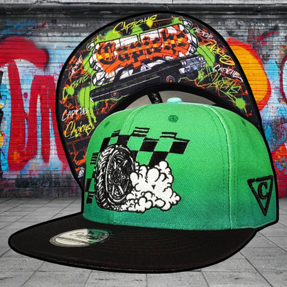 Two colorful caps with graphic designs against a graffiti-covered wall.