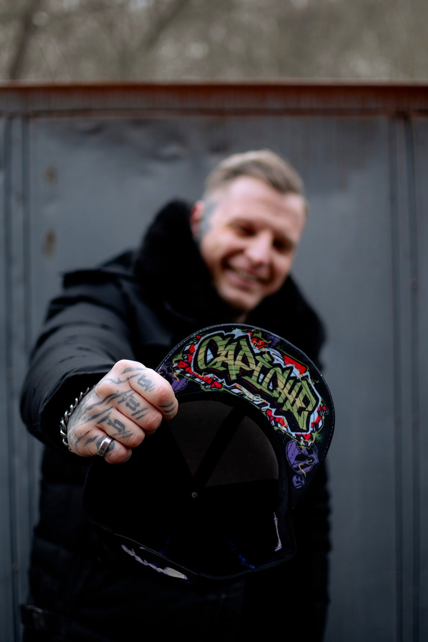 Man tattoo model standing outside smiling and holding the Freestyler snapback hat with Capiche written on it