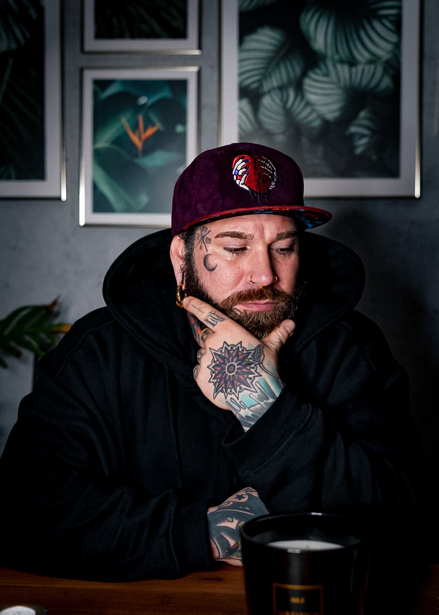 Tattoo model sitting on a table wearing a suede snapback from Capiche Caps