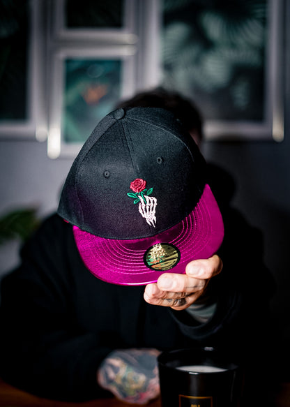 Man holding the black snapback with pink crackling metallic visor to show to the camera