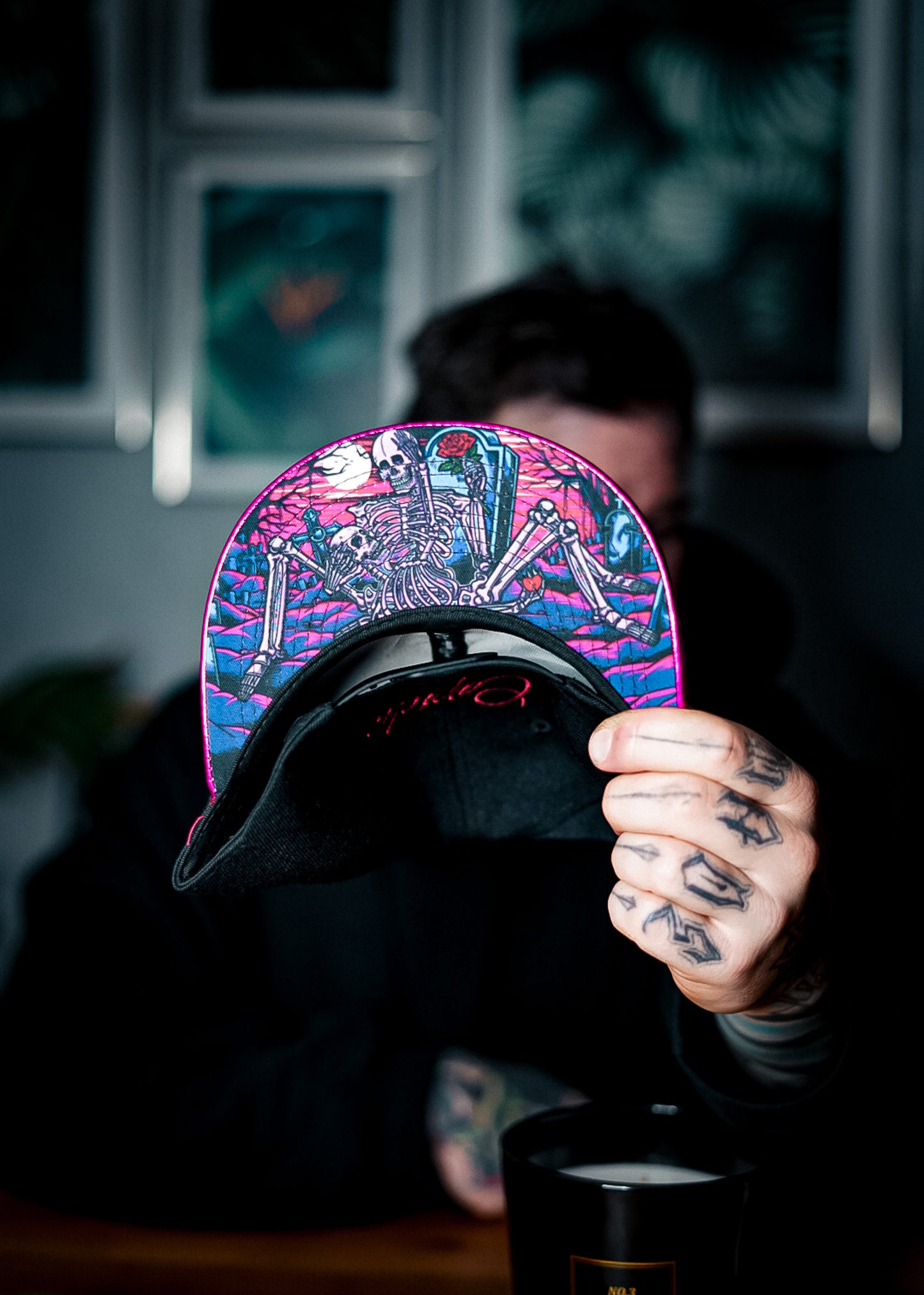 Man with tattoos in his hands holding the Valentine snapback and showing the bottom design with two skeletons on a graveyard